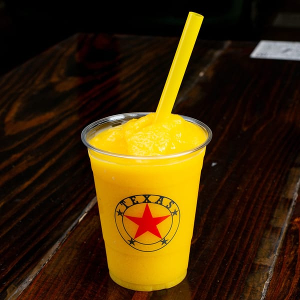 A bright yellow frozen drink with a yellow straw in a clear cup with a red star logo.