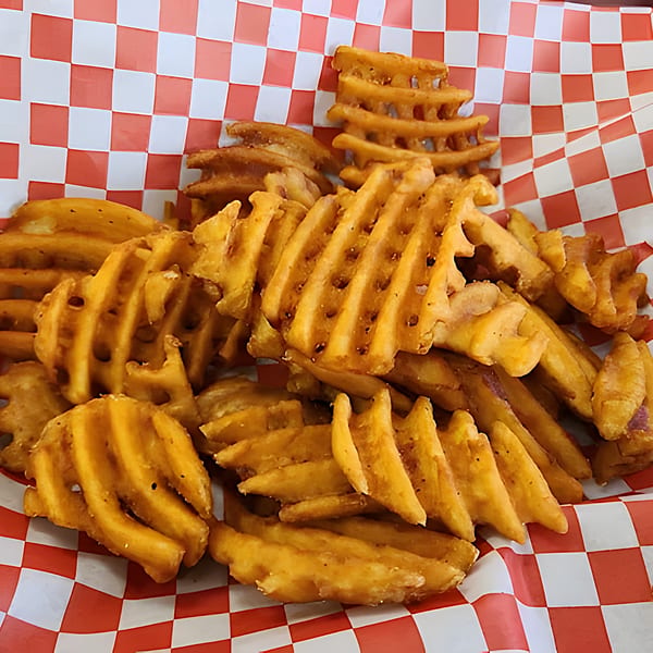 A basket of golden brown waffle fries, seasoned and served in a red and white checkered paper liner.