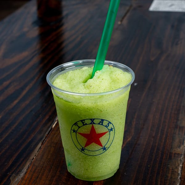 A green frozen drink with a Texas logo and a green straw on a wooden table.