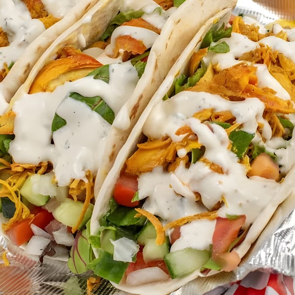 Close-up of Gyro Queen's chicken gyros with lettuce, tomatoes, cucumbers, and white sauce.