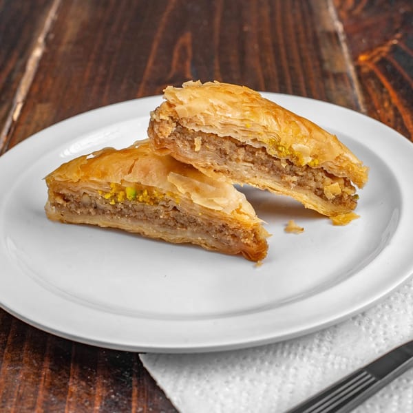 Two pieces of baklava with flaky pastry and nut filling on a white plate.