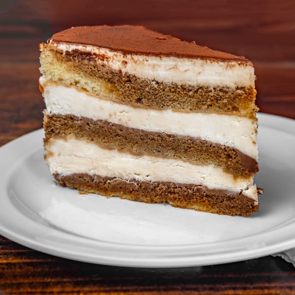 A slice of tiramisu cake with layers of coffee-soaked sponge and cream, dusted with cocoa.
