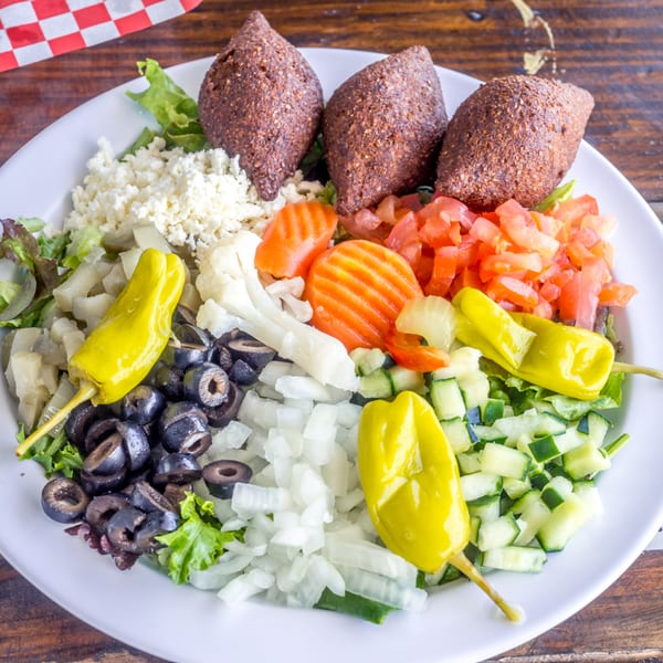 A vibrant Mediterranean salad with kibbeh, feta, olives, tomatoes, cucumbers, and pickled peppers.