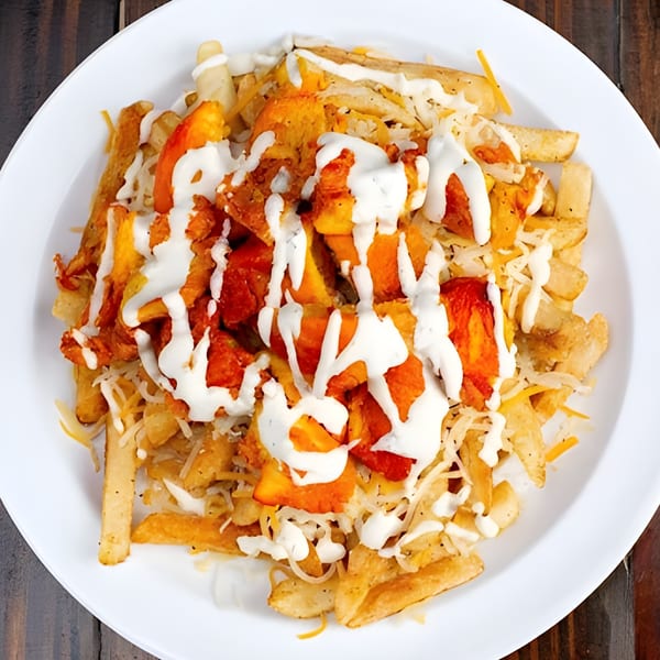 Gyro Queen's loaded fries with chicken, shredded cheese, and white sauce on a white plate.