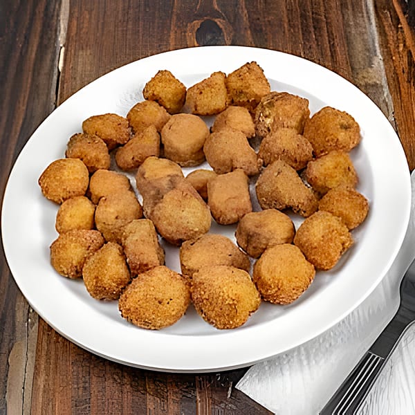 A white plate filled with golden-brown fried falafel pieces on a rustic wooden table.